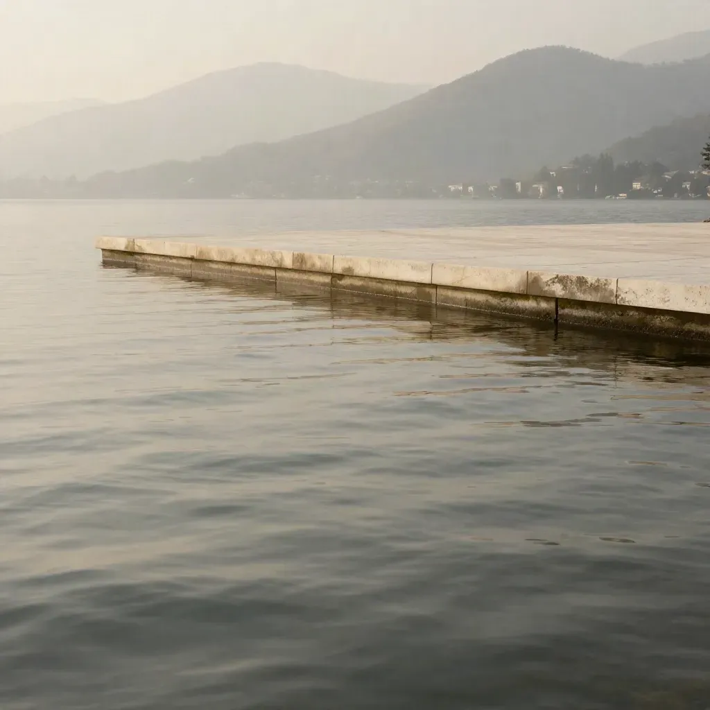 Terrazza in pietra sul lago di Como, acqua calma e colline sfumate nella foschia.